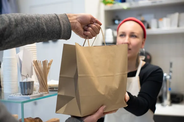 Empleada de un restaurante entregando una bolsa de comida para llevar